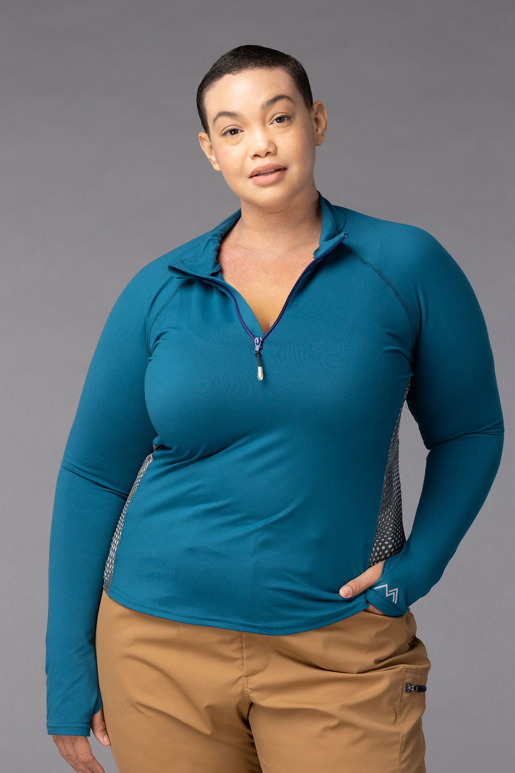 Woman looking at the camera wearing a quarter-zip long sleeve shirt and hiking pants.